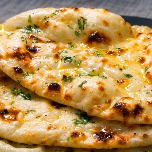 Golden-brown naan bread, brushed with butter and sprinkled with fresh herbs, stacked on a dark plate.