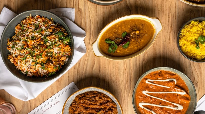 Overhead view of various Indian dishes, including rice, dal, and curries, on a wooden table.