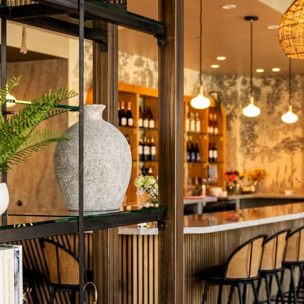 A modern bar area with rattan stools, hanging lights, and a nature-themed mural.