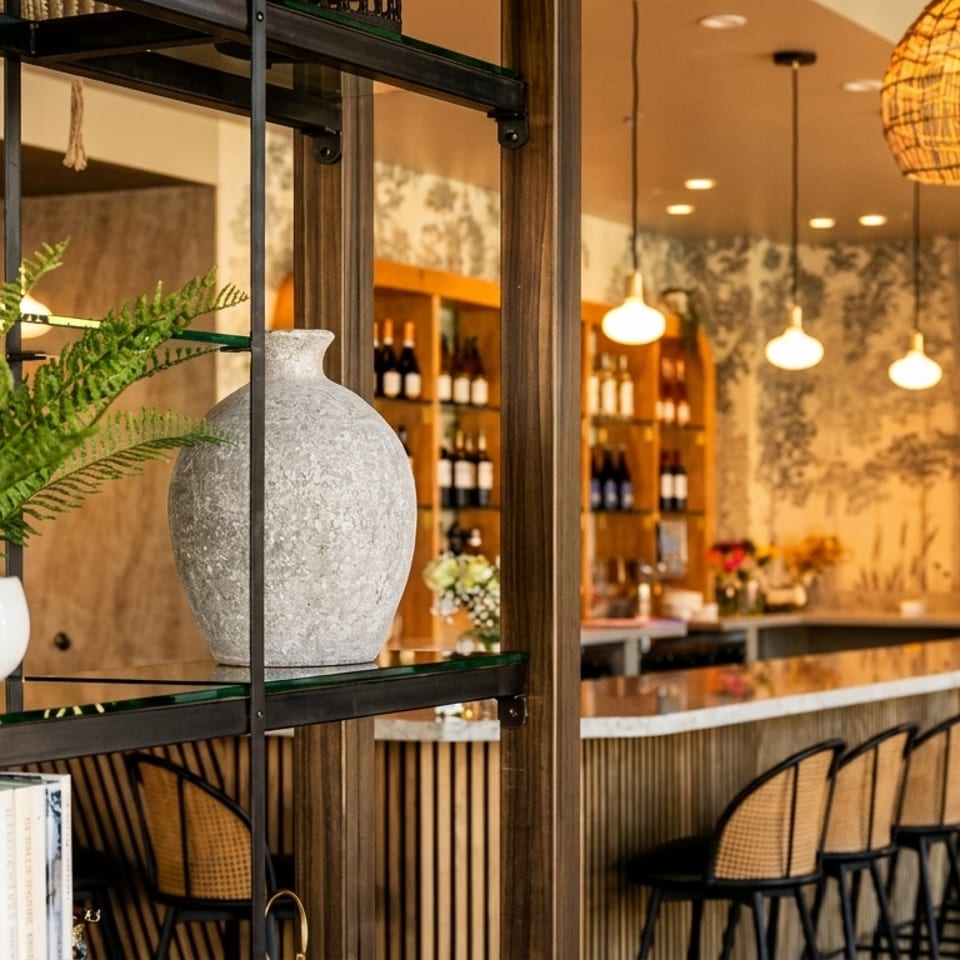 A modern bar area with rattan stools, hanging lights, and a nature-themed mural.