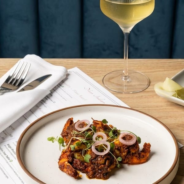 Indian dishes of shrimp and meat, a glass of white wine, and a menu on a wooden table.