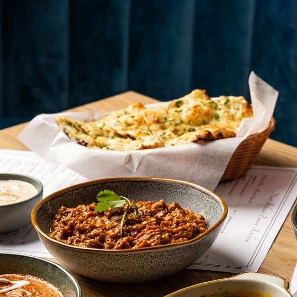 Indian dishes, including naan, curries, rice, and a pink lassi, on a wooden table.