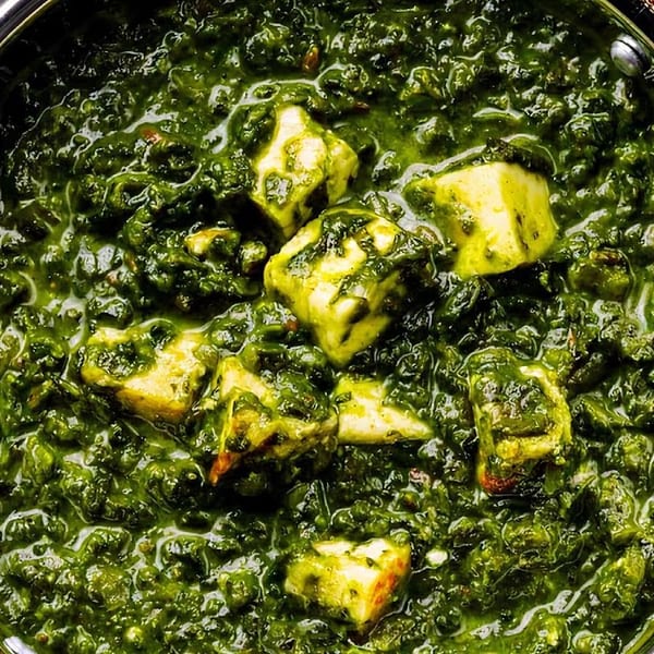 Close-up of Palak Paneer, a vibrant green spinach curry with cubes of paneer cheese in a metal bowl.