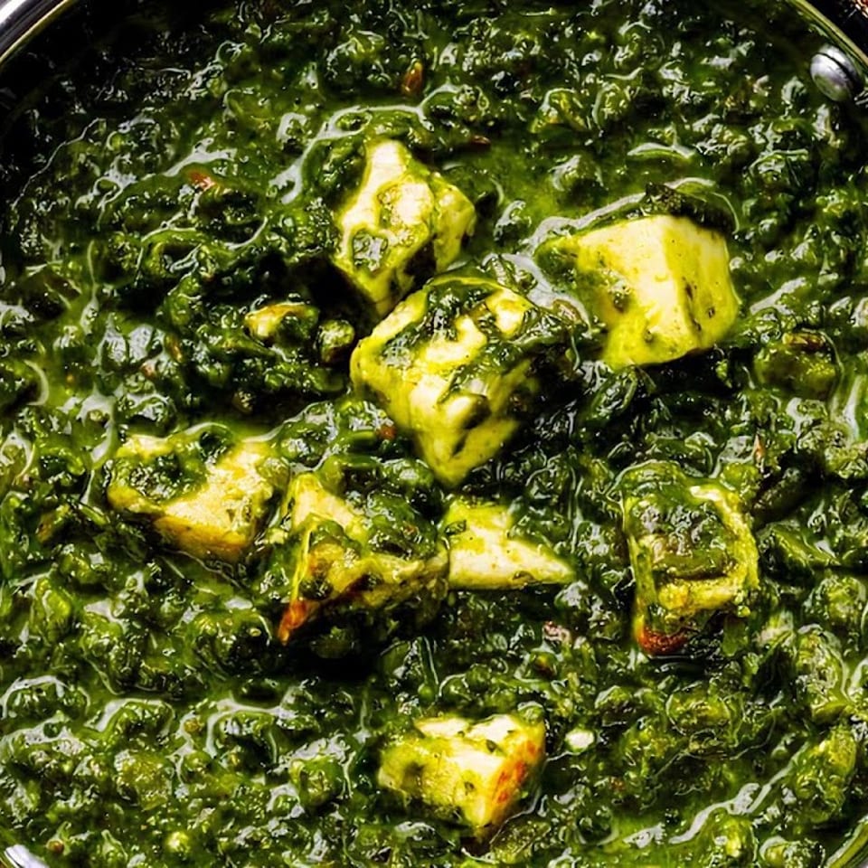 Close-up of Palak Paneer, a vibrant green spinach curry with cubes of paneer cheese in a metal bowl.