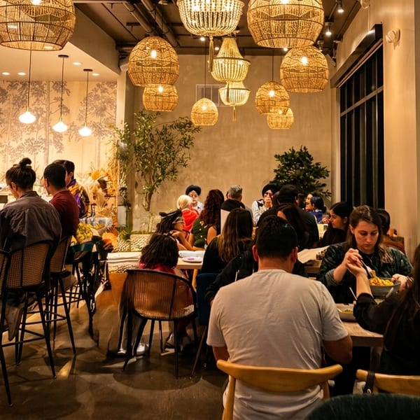 Diners enjoying meals and drinks at a lively, warmly lit restaurant with woven pendant lights.