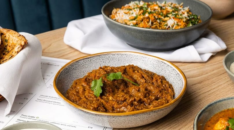 Indian dishes on a wooden table, including a bowl of curry, rice, and naan bread.