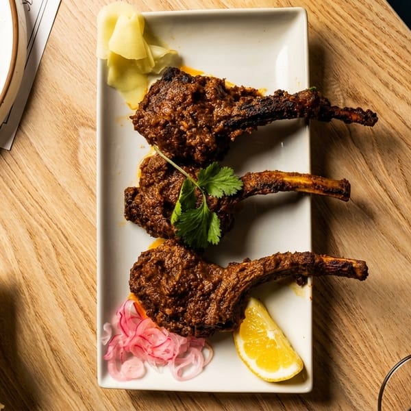 Three lamb chops with cilantro, pickled onions, and lemon on a white plate.