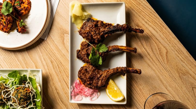 Three lamb chops with cilantro, pickled onions, and lemon on a white plate.