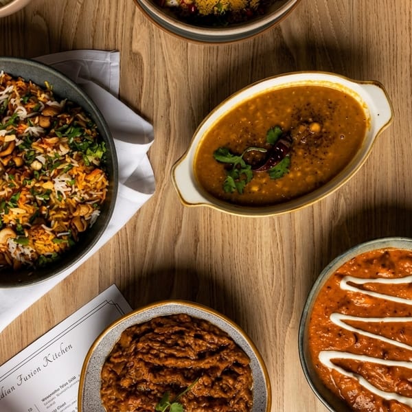 An overhead view of various Indian dishes, including rice, curries, and dal, on a wooden table.