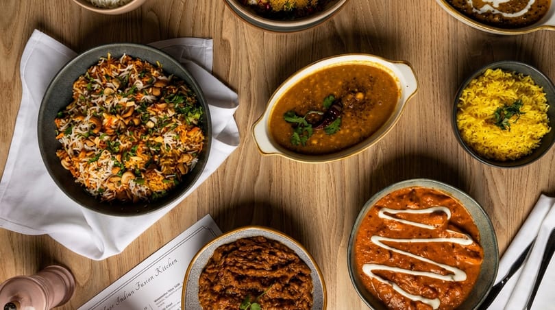 An overhead view of various Indian dishes, including rice, curries, and dal, on a wooden table.