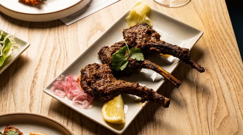 Three lamb chops with cilantro, pickled onions, lemon, and ginger on a white plate.